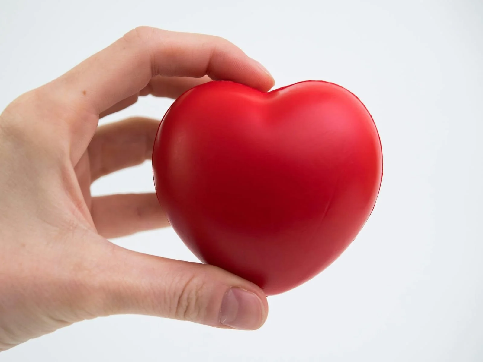 Hand hält eine rote, herzförmige Zierkugel vor einem weißen Hintergrund.