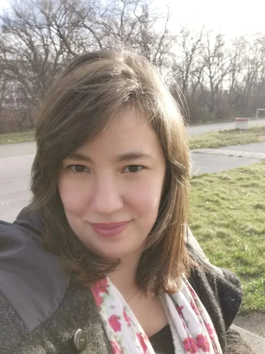 Nahaufnahme einer Frau mit braunen Haaren, die draußen im Sonnenlicht lächelt.