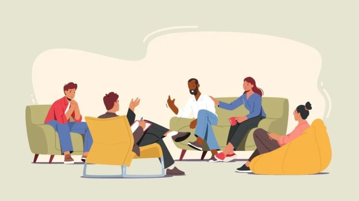 Eine Gruppe von fünf Menschen in einer entspannten Diskussion in einem Wohnzimmer, sitzend auf Sofas und Sesseln.