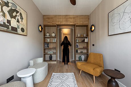 Ein Wohnzimmer mit modernen Möbeln, einer Person, die in die Tür geht, Wandbildern und einem Holzregal.