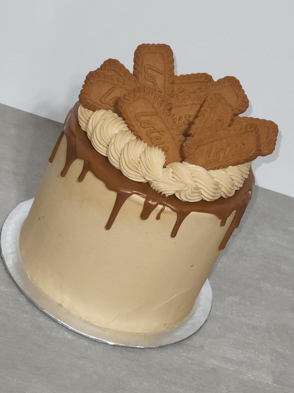 A tall, cylindrical birthday cake with beige frosting and chocolate drip decoration, topped with oreo cookies and beige piping cream.