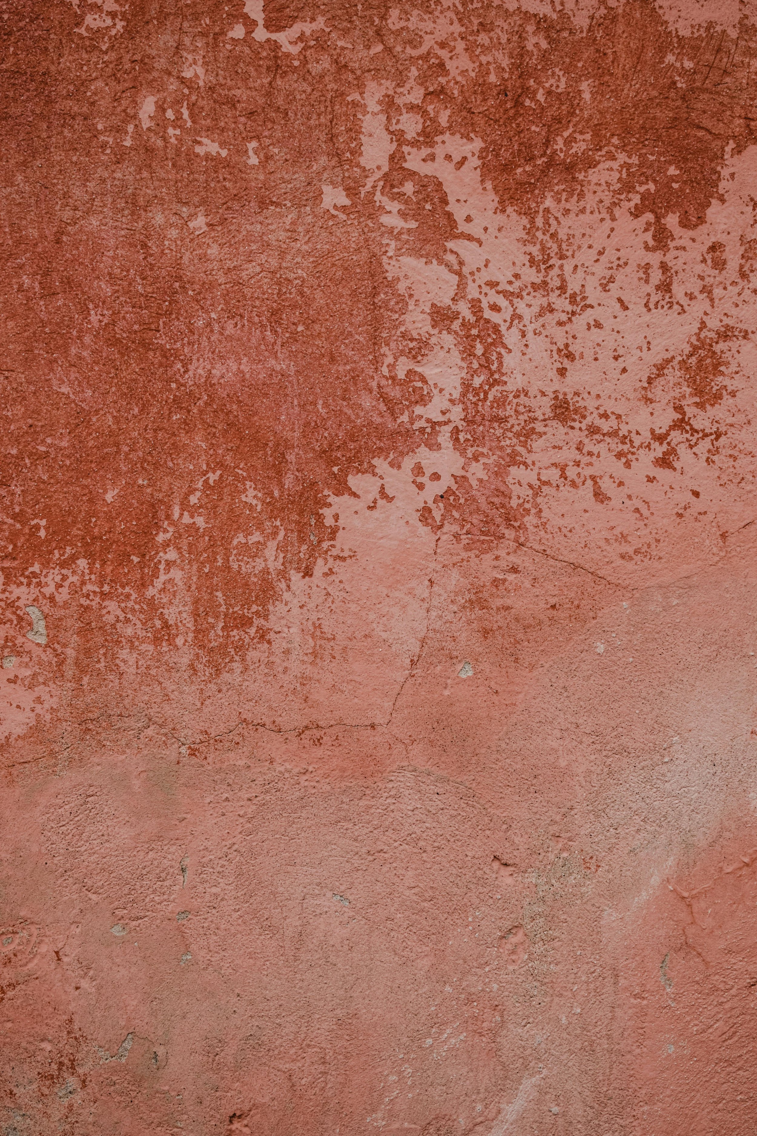 Close-up of a weathered pink wall with peeling paint and cracks.