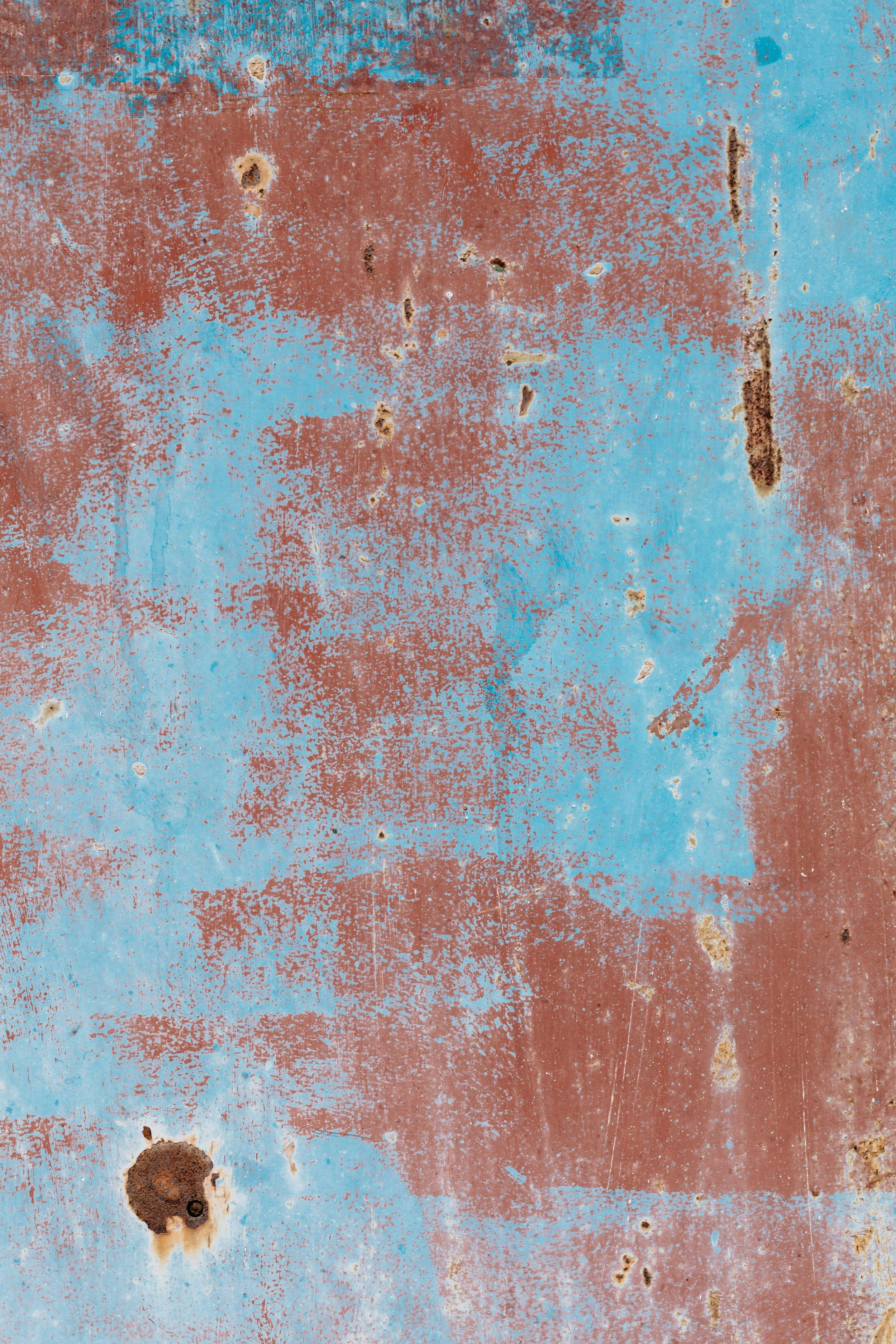 A close-up of a weathered metal surface with blue and rust-colored paint, exhibiting rust spots, scratches, and peeling paint.