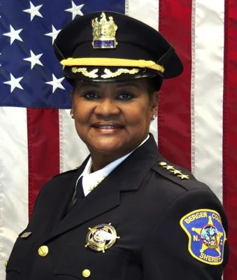 Police officer in uniform standing in front of an American flag.