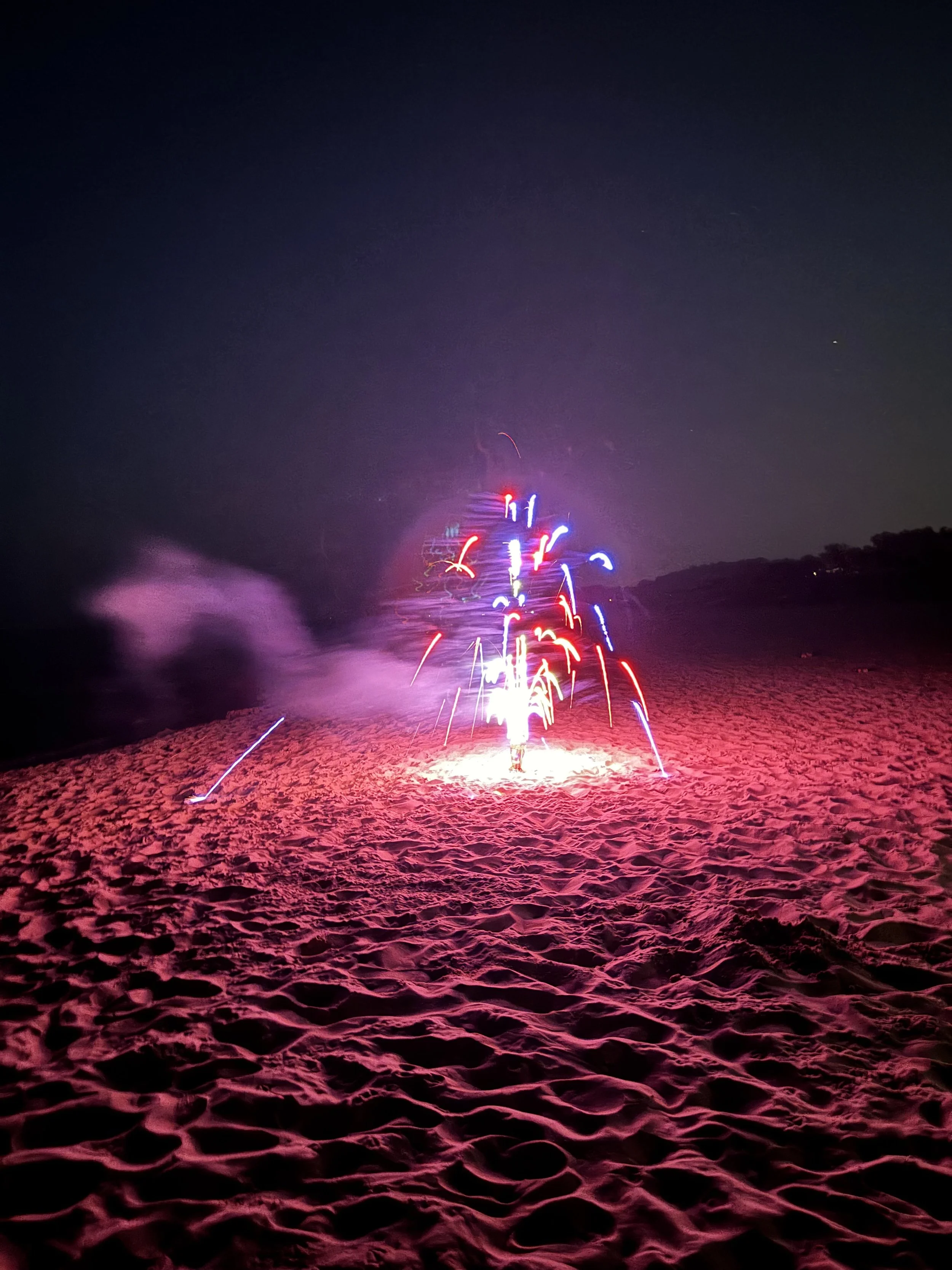 Fireworks on a sandy beach at night, with colorful sparks illuminating the dark sky.