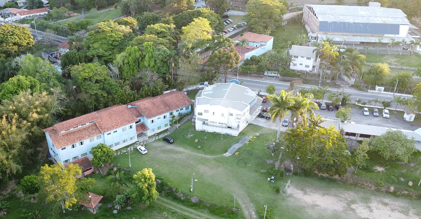 Vista aérea da comunidade magnificat de um bairro com árvores, casas, uma área de lazer com gramado e alguns veículos estacionados.