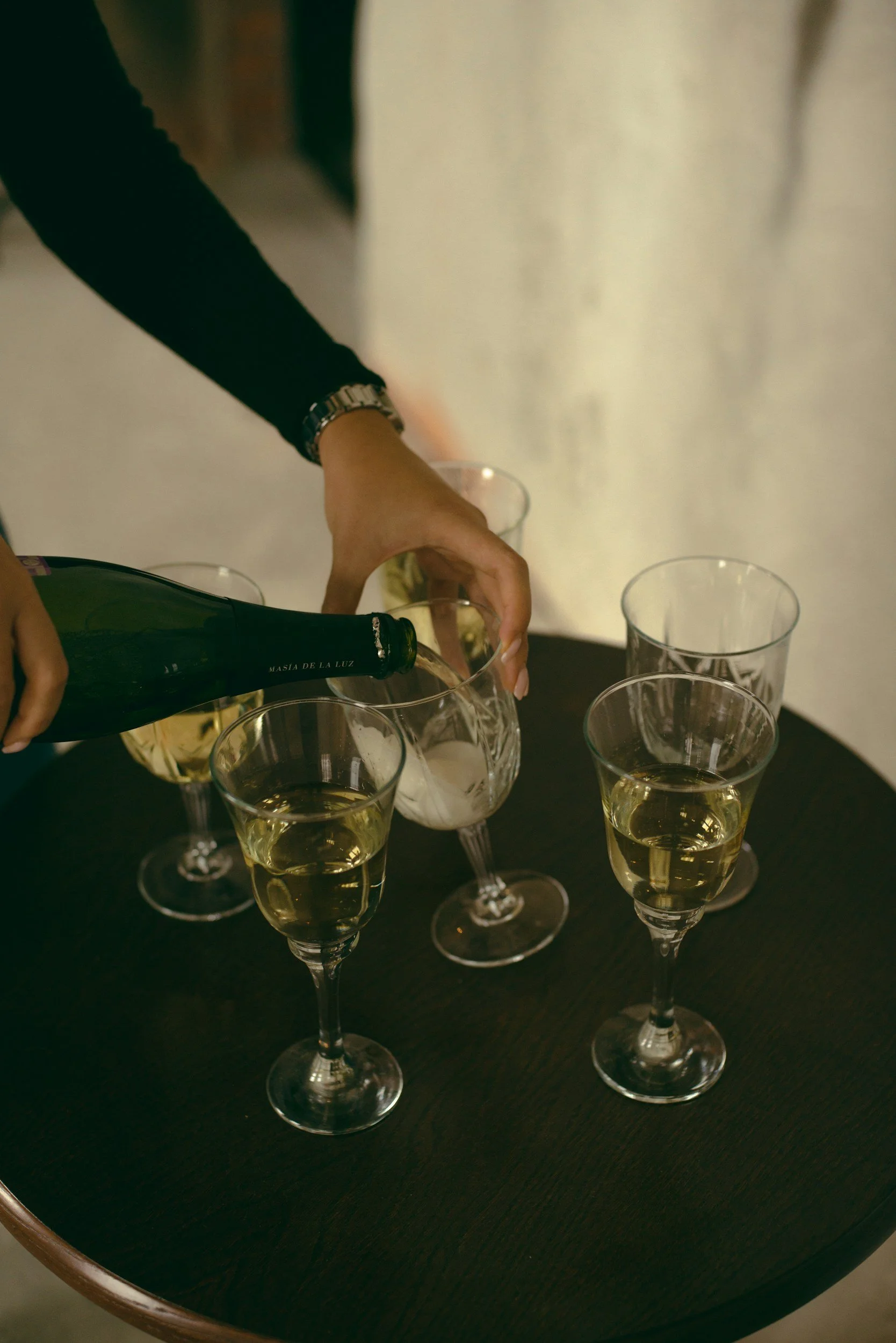 Person pouring champagne into glass at a table with several filled champagne flutes.