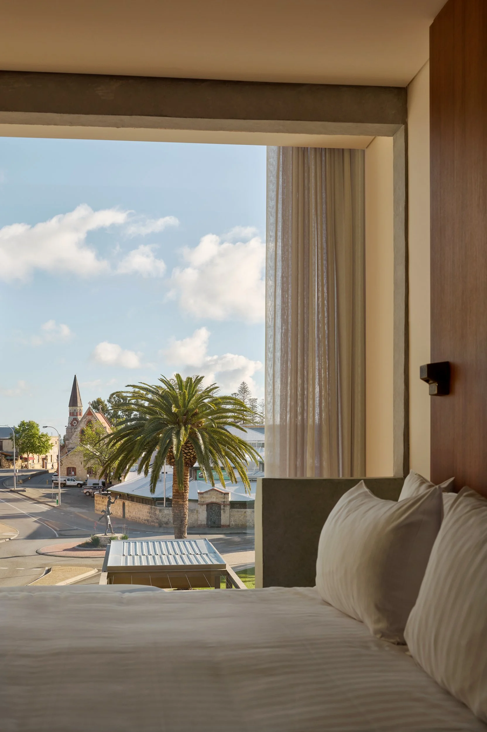 View from a hotel room window showing a palm tree, a church with a steeple, and a street scene with cars and a pedestrian