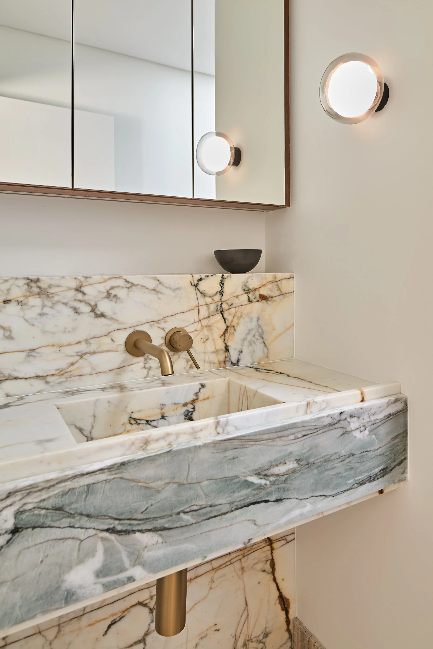 A bathroom vanity with a marble sink and backsplash, a wall mirror, and two round wall-mounted lights.