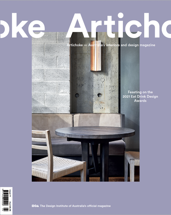 Cover of Artichoke magazine featuring a modern interior with a round wooden table, two chairs, a beige bench, and textured walls with graffiti and a vertical copper light fixture.