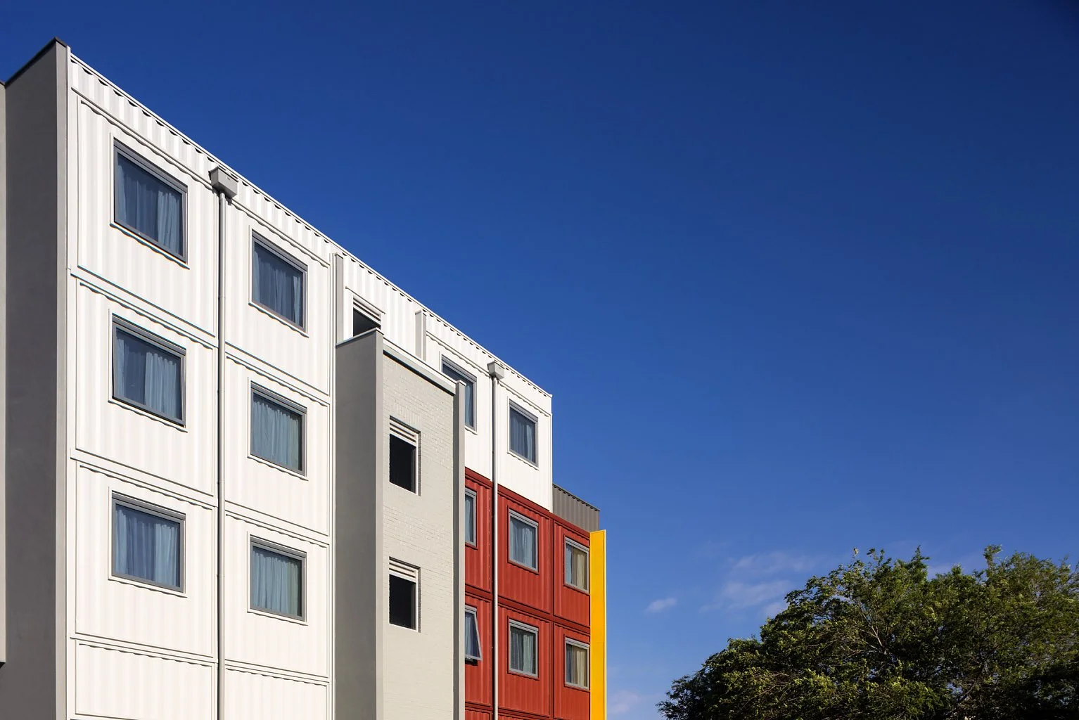 Modern multi-story building with colorful facade, blue sky, and green trees.