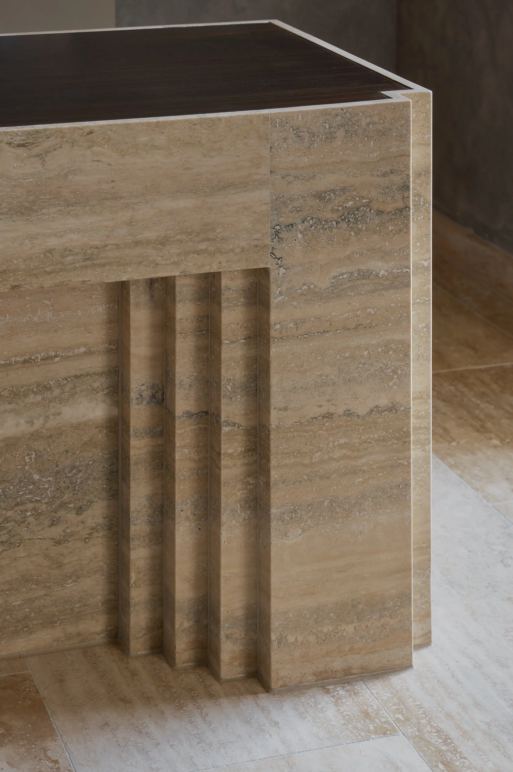 Close-up of a marble or stone countertop and supporting pillar with inset grooves on the side, in a neutral-toned interior.