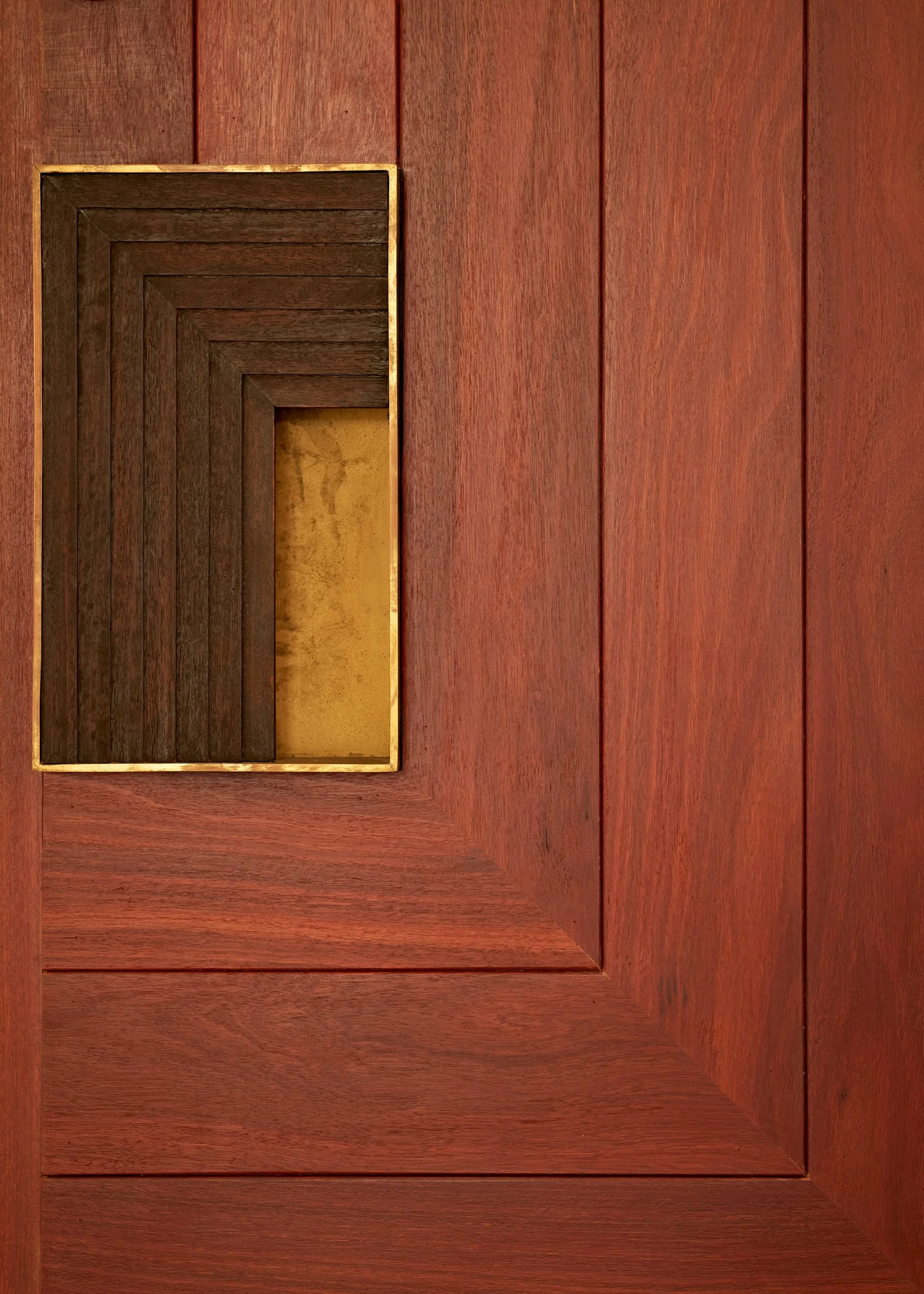 Close-up of a wooden surface with a rectangular inset, framed with light-colored wood, containing a smaller, darker wooden box with multiple layers, and a gold-colored backing.