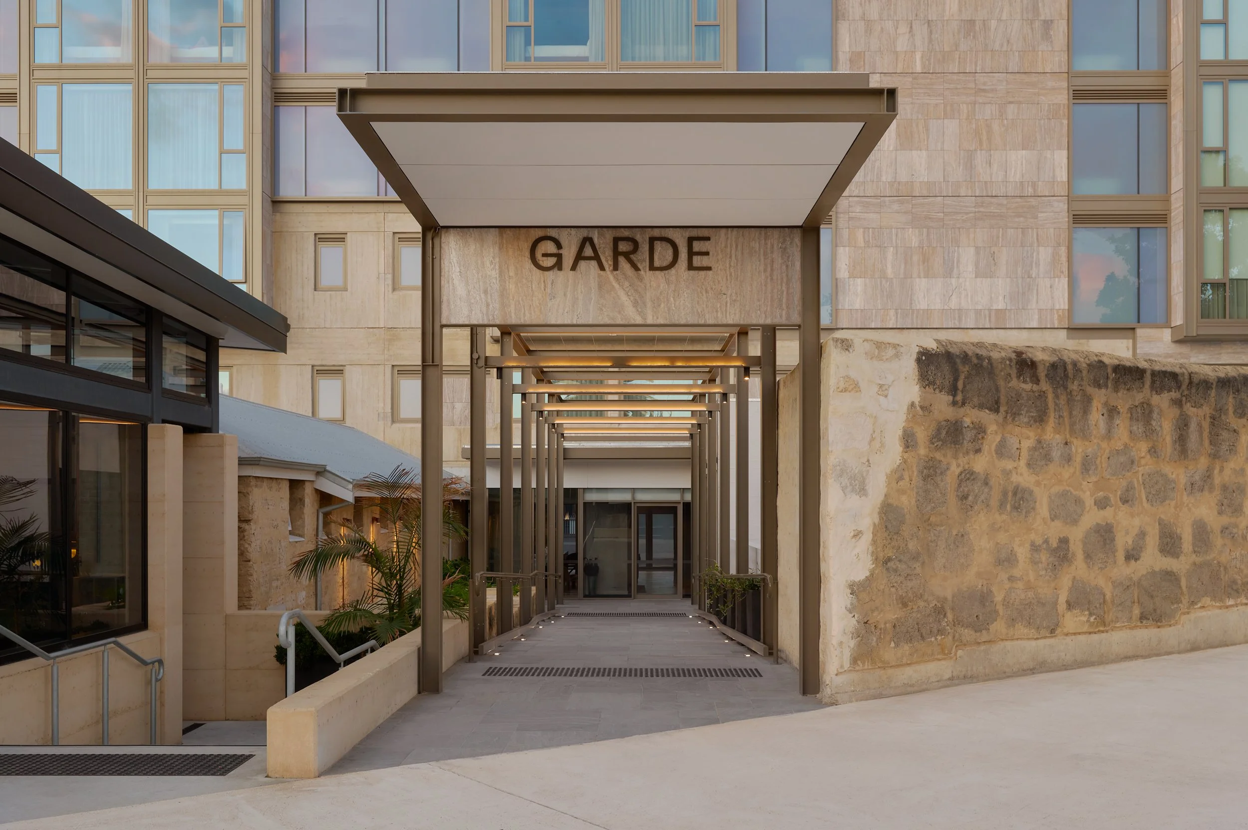 Modern building entrance with a covered walkway, signage reading 'GARDE,' and glass windows.