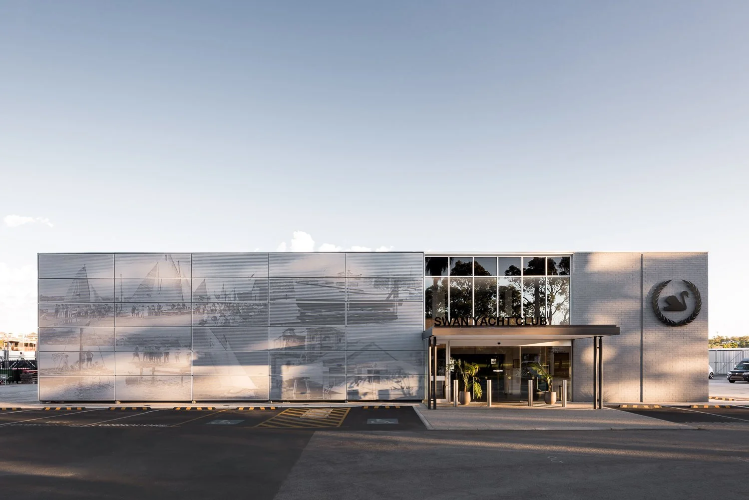 Exterior of Swan Yacht Club building with reflective glass facade, yacht images, and logo on brick wall in bright daylight.