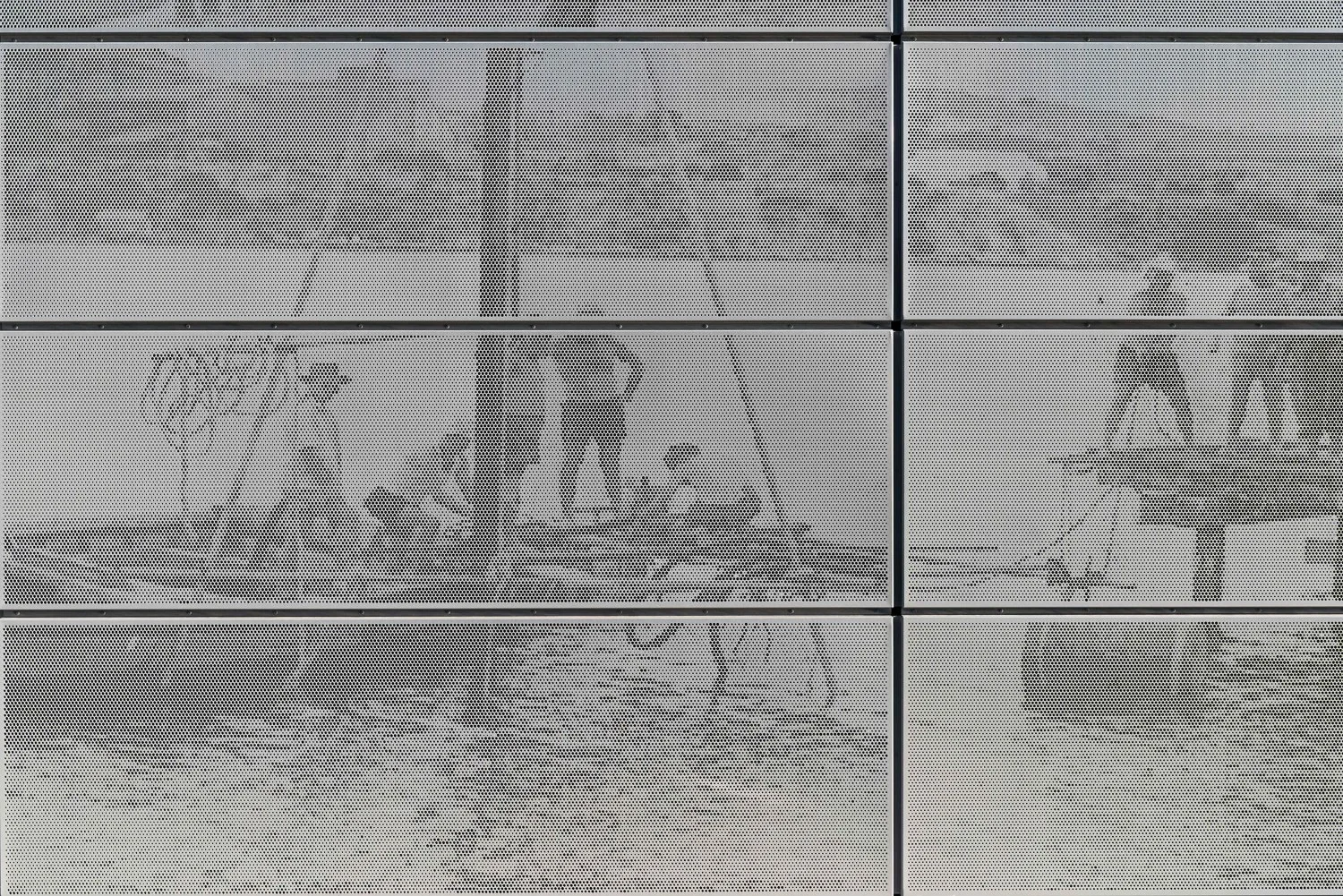 Reflection of two people working at a table seen through a perforated metal wall.