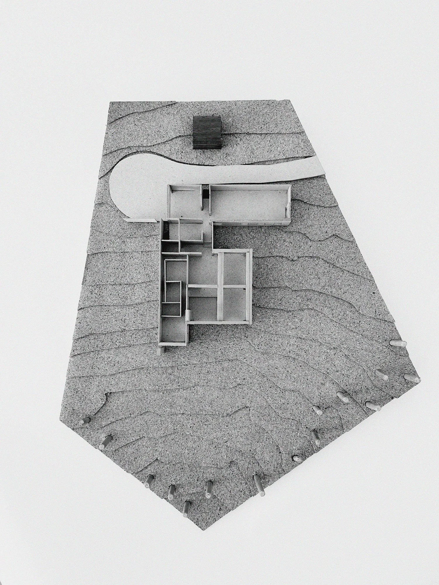 Architectural model of a building with a detailed landscape, featuring multiple rooms, a curved pathway, and textured terrain.