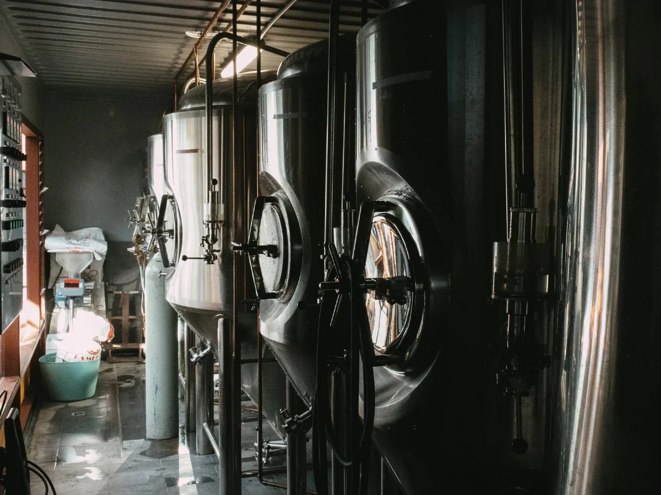 Interior view of a brewery or industrial facility with large stainless steel fermentation tanks.