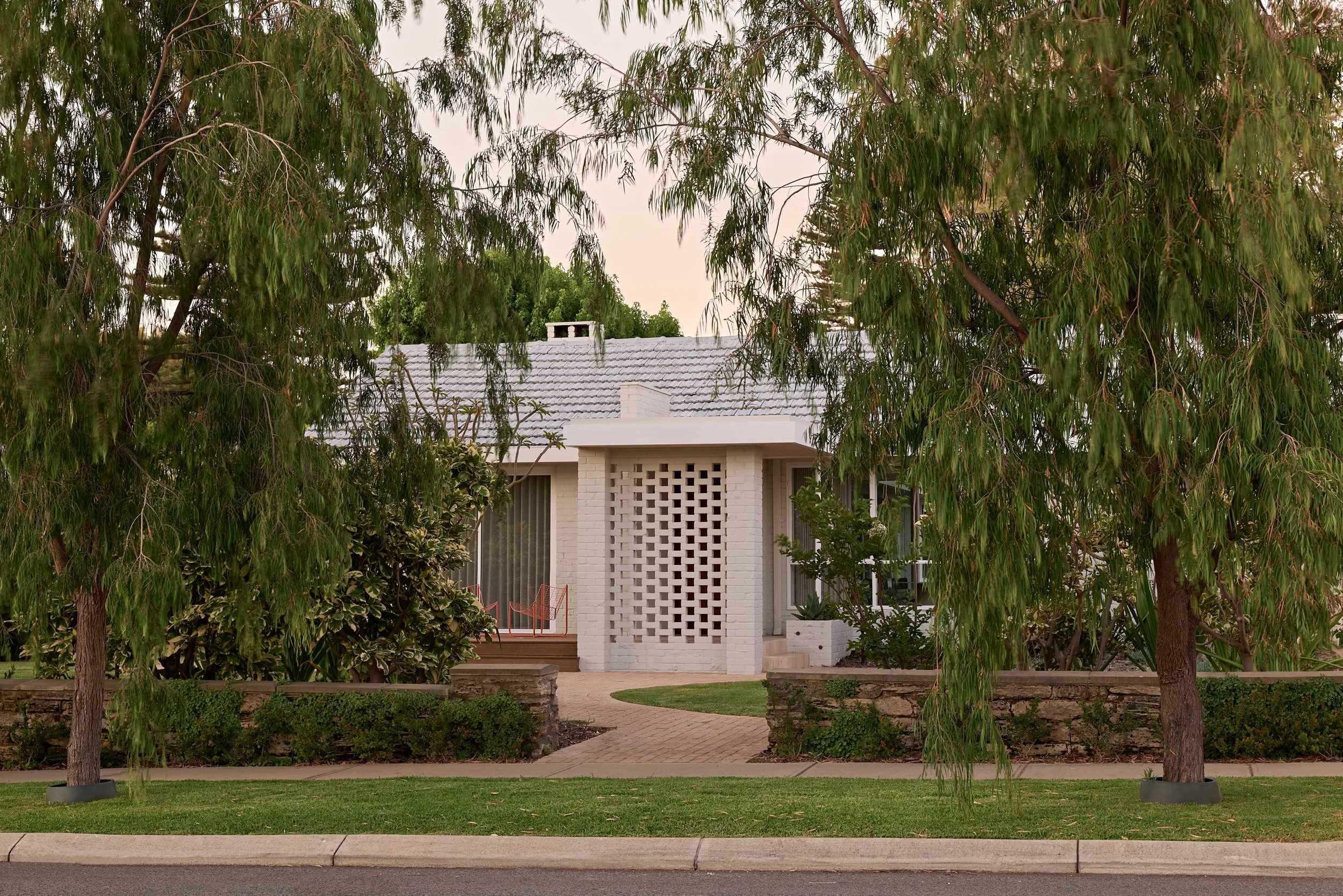 A house partially obscured by leafy trees with a brick walkway leading to the entrance.