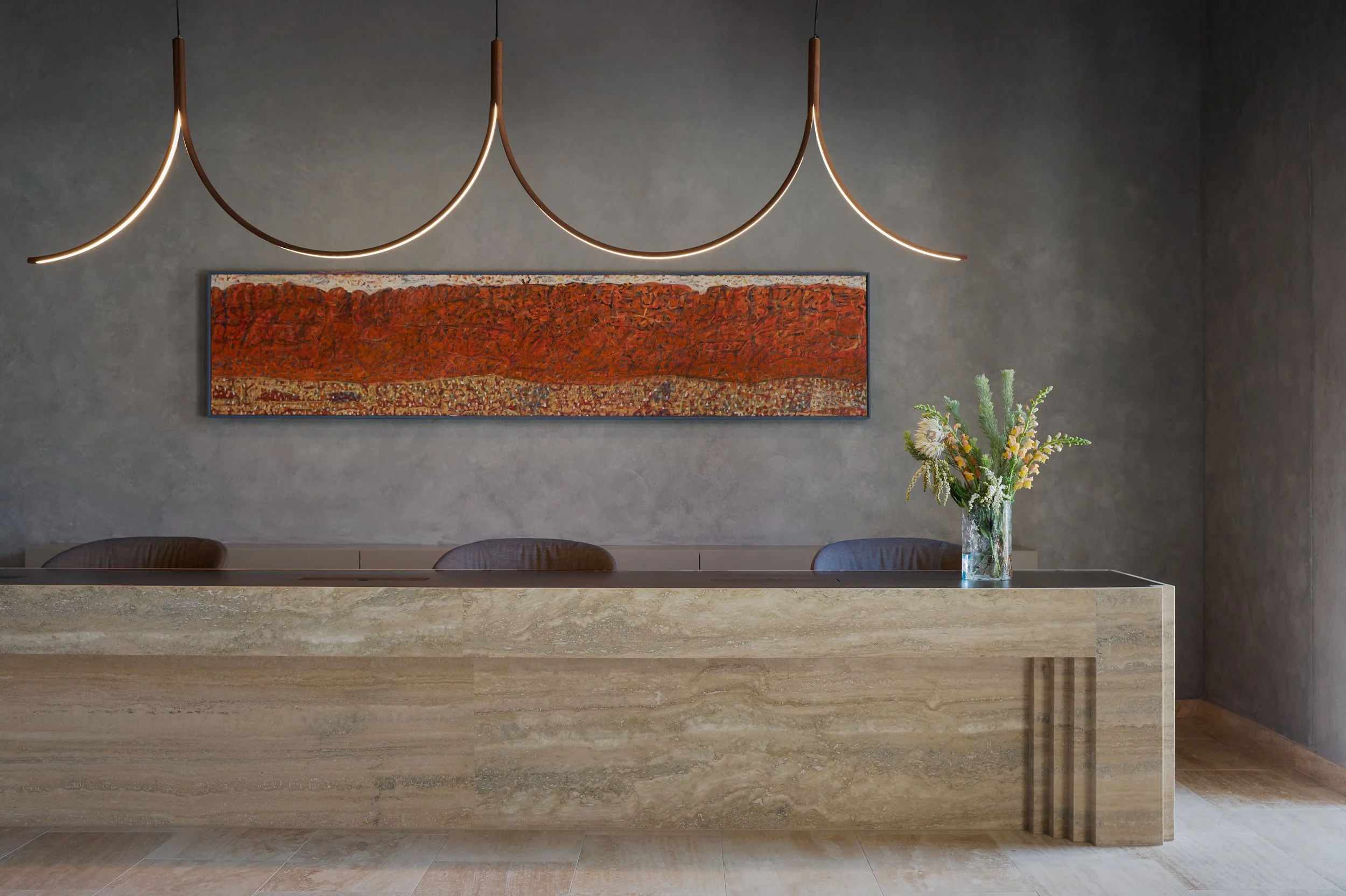 Modern reception desk with a vase of flowers, dark gray textured wall, colorful abstract painting, and unique hanging light fixtures in a minimalist interior.