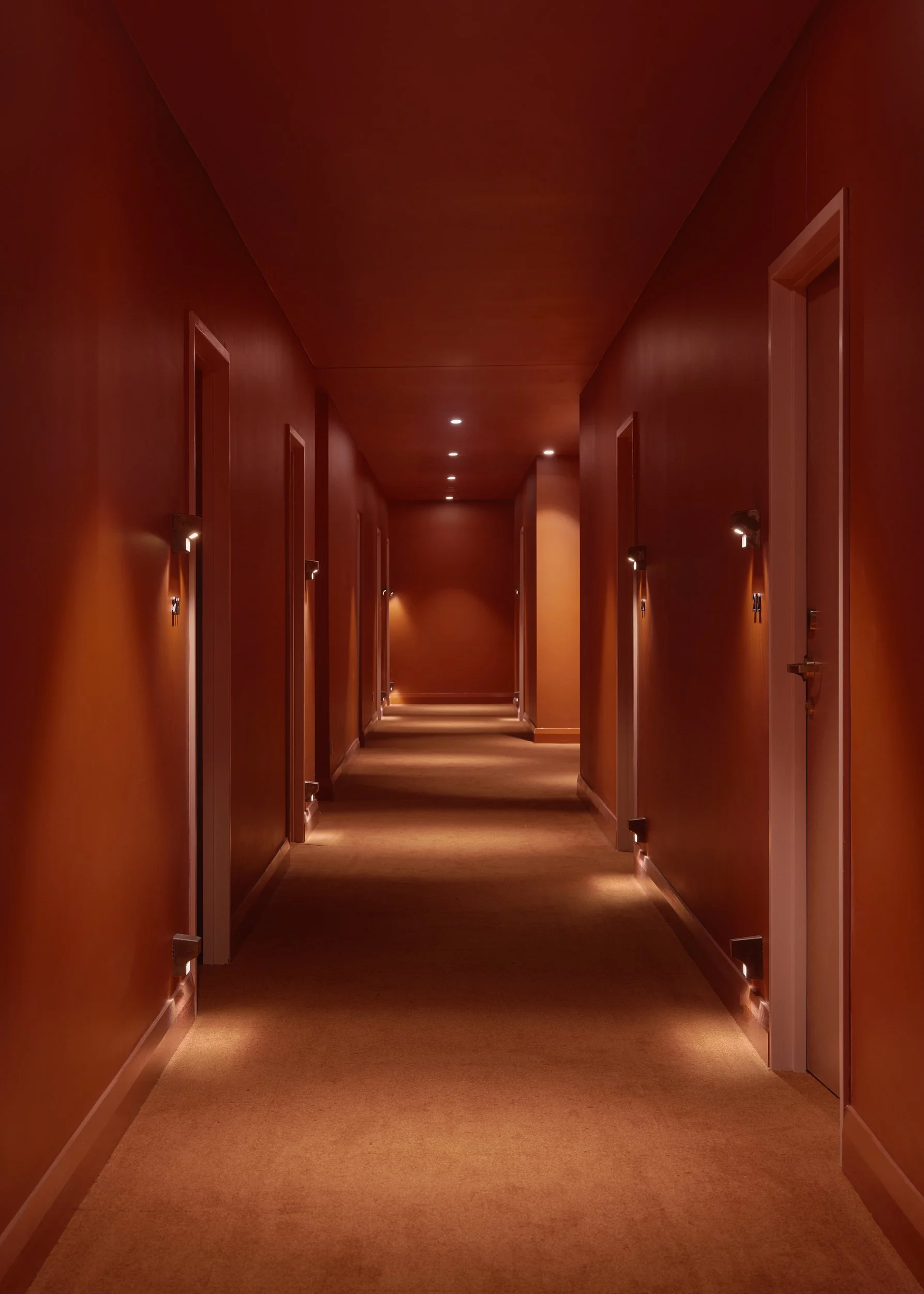 Long hallway with closed doors on both sides, warm lighting, and a carpeted floor.