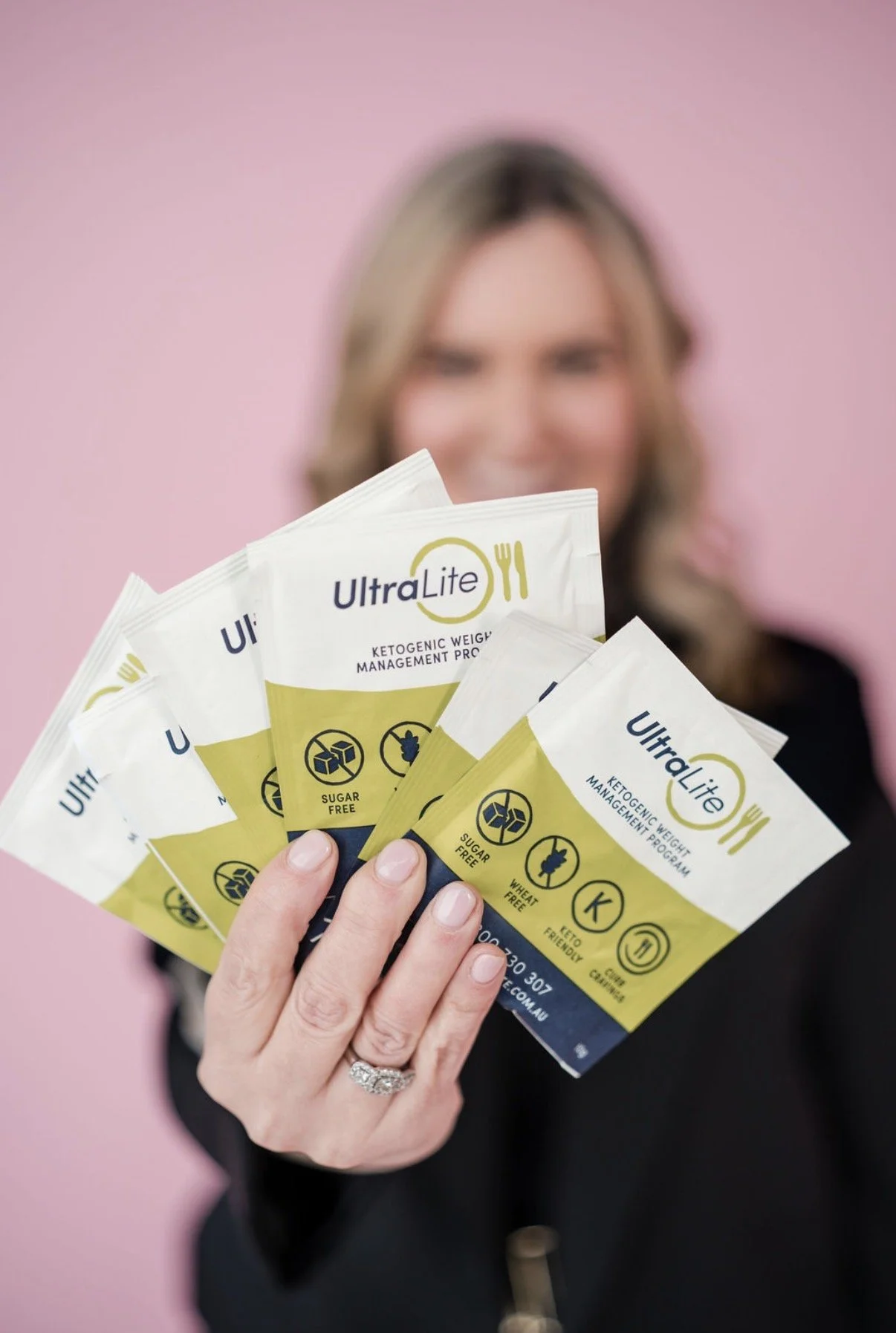 A woman holding several packets of UltraLite ketogenic weight management program, with a pink background.