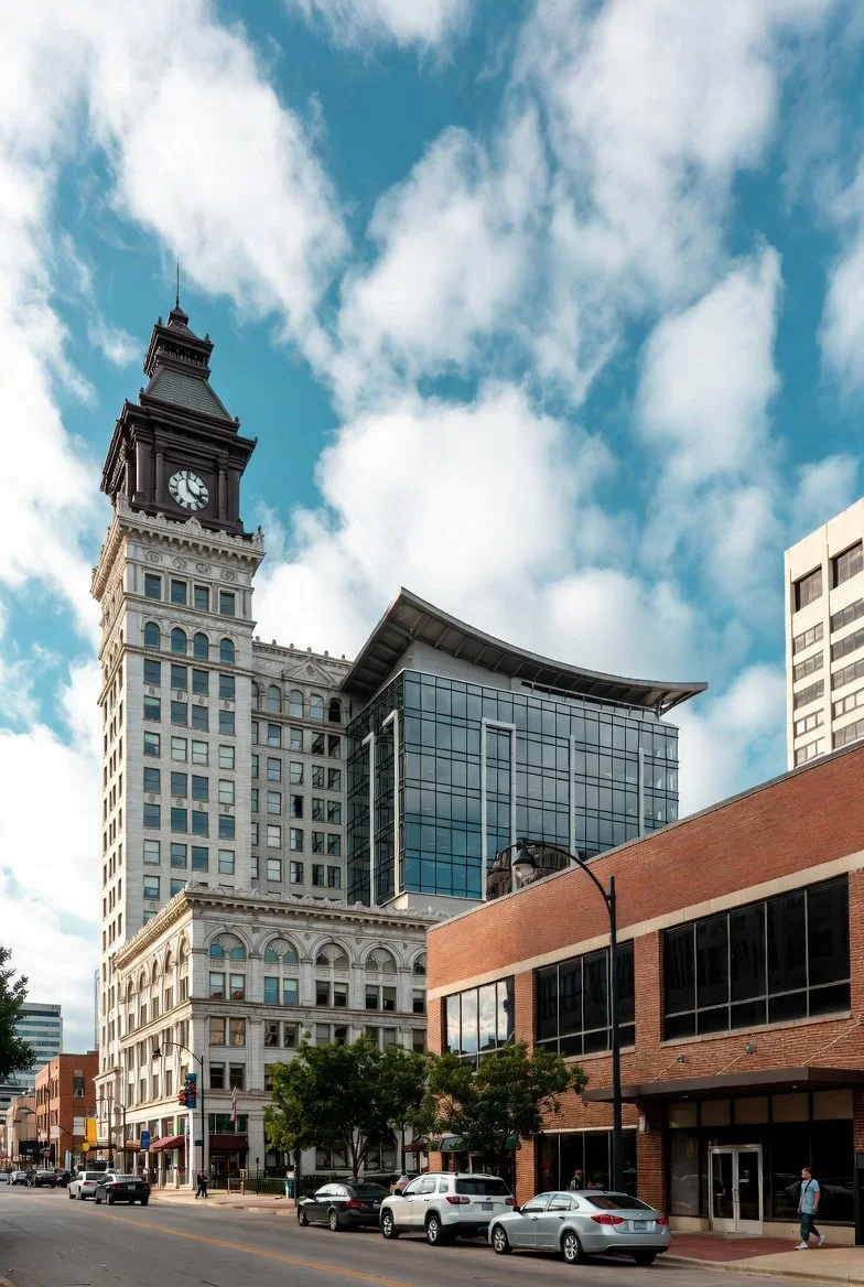 A circular illustration of a city skyline with tall buildings and trees in the foreground, a body of water in front, and a full moon or sun in the sky.