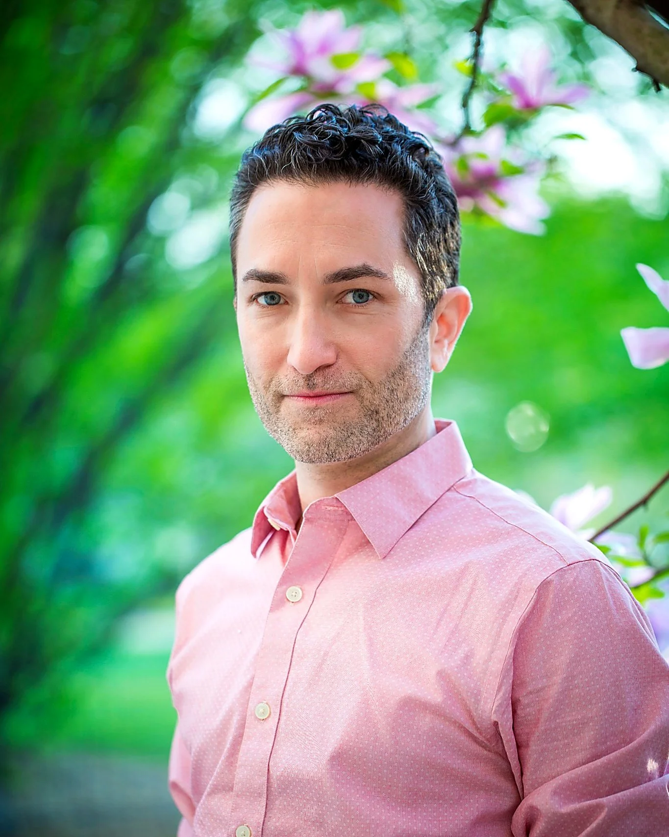 Headshot of Tom Sunshine wearing a pink short in front of greenery
