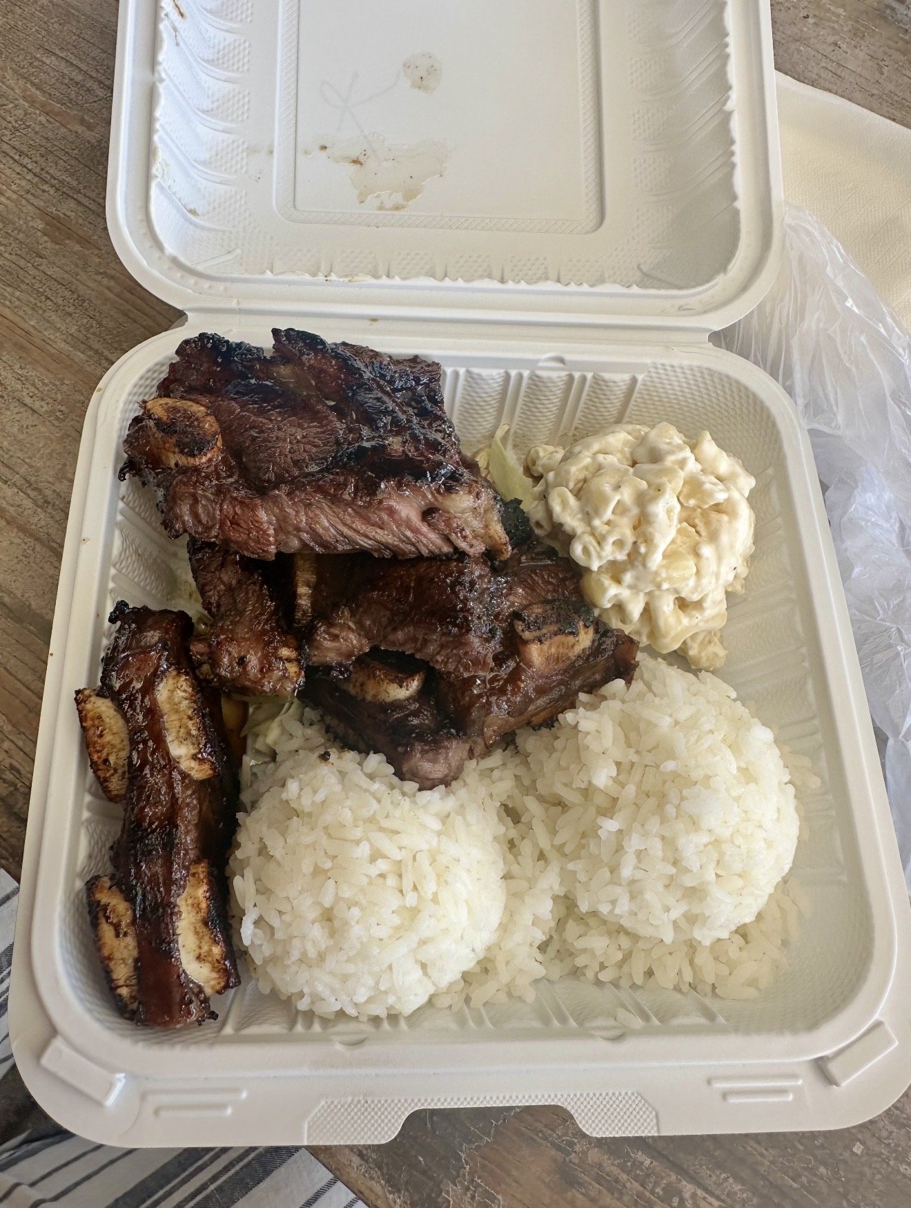 Box containing cooked ribs, mashed potatoes, macaroni salad, and barbeque spare ribs.