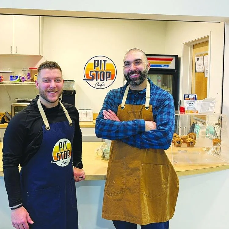 Jeff Hull and Michael Zuniga, co-owners of Pit Stop Cafe in Fairbanks, standing behind the cafe counter wearing aprons and smiling at the camera.