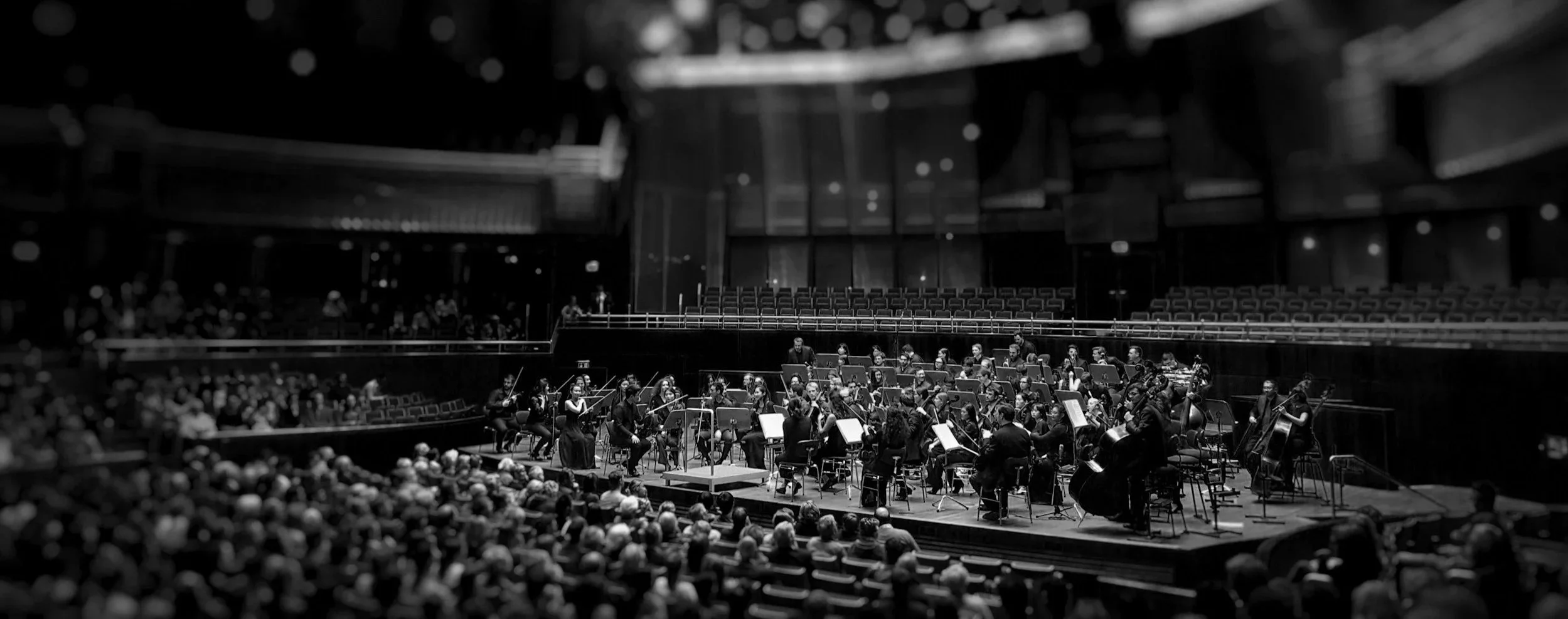 An orchestra performing on stage in a concert hall with an audience watching.