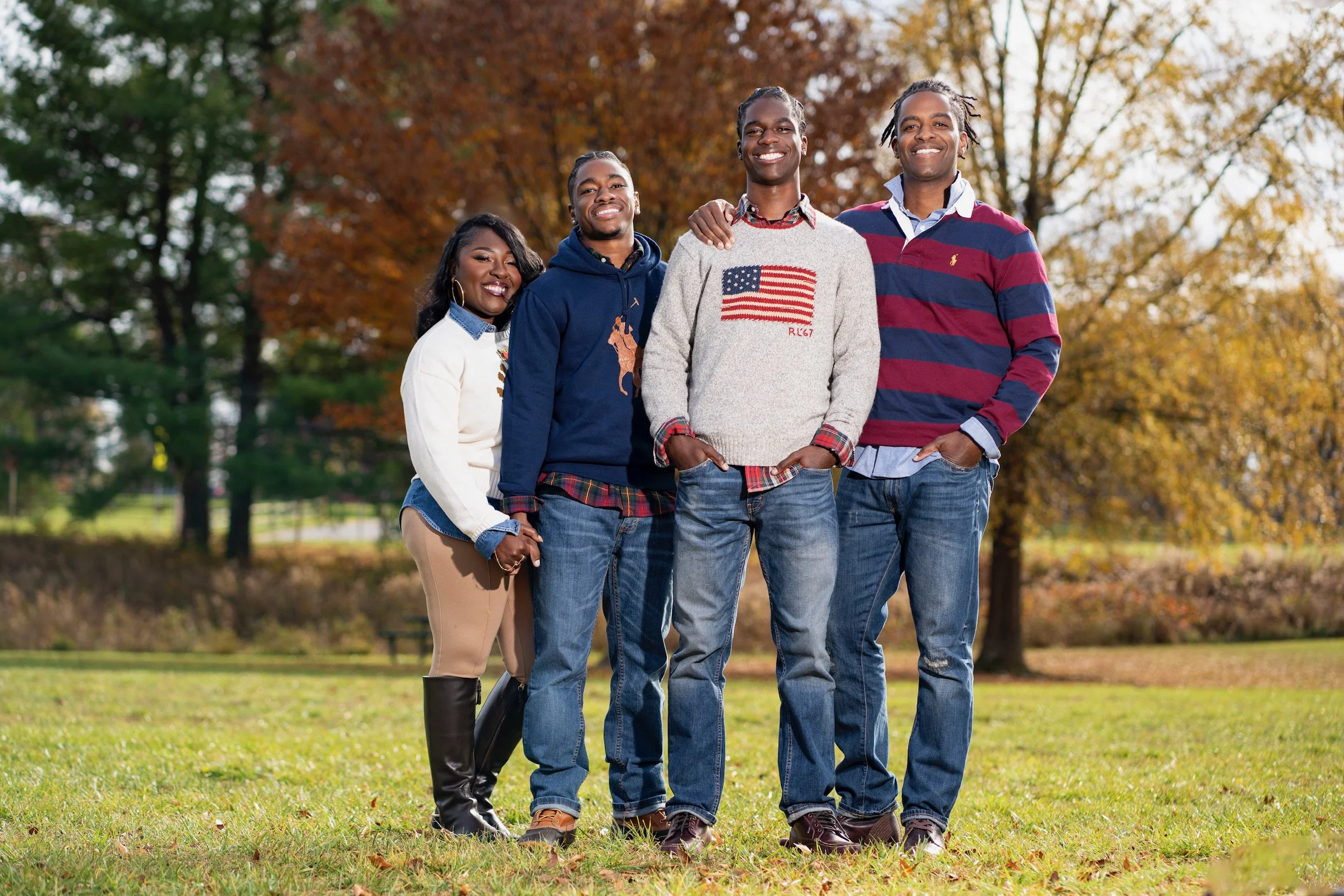 A group of five friends standing outdoors in a park with autumn trees, smiling and posing for the camera.