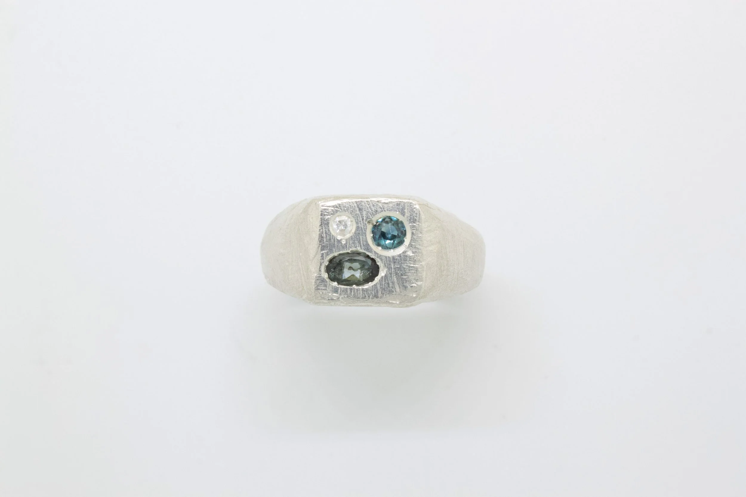 Silver ring with three embedded gemstones set on a plain white background.