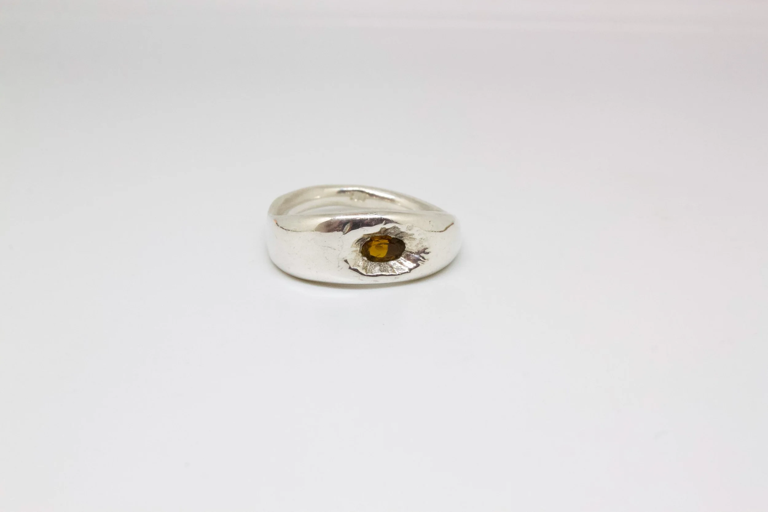 Silver ring with a small amber gemstone on a white background.