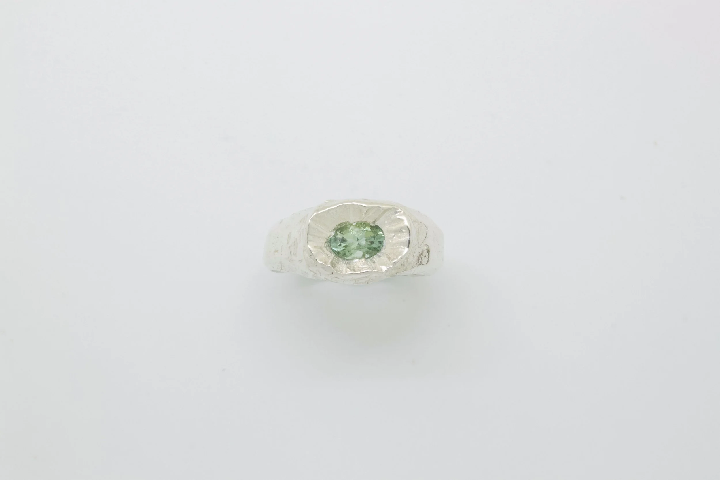 Silver ring with a green oval gemstone in the center, on a white background.