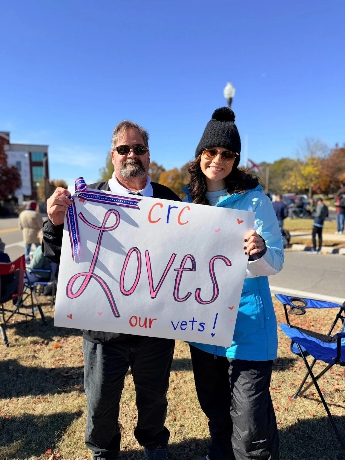 Two people holding a sign that says 'CRC Loves our vets!' at an outdoor event on a sunny day.
