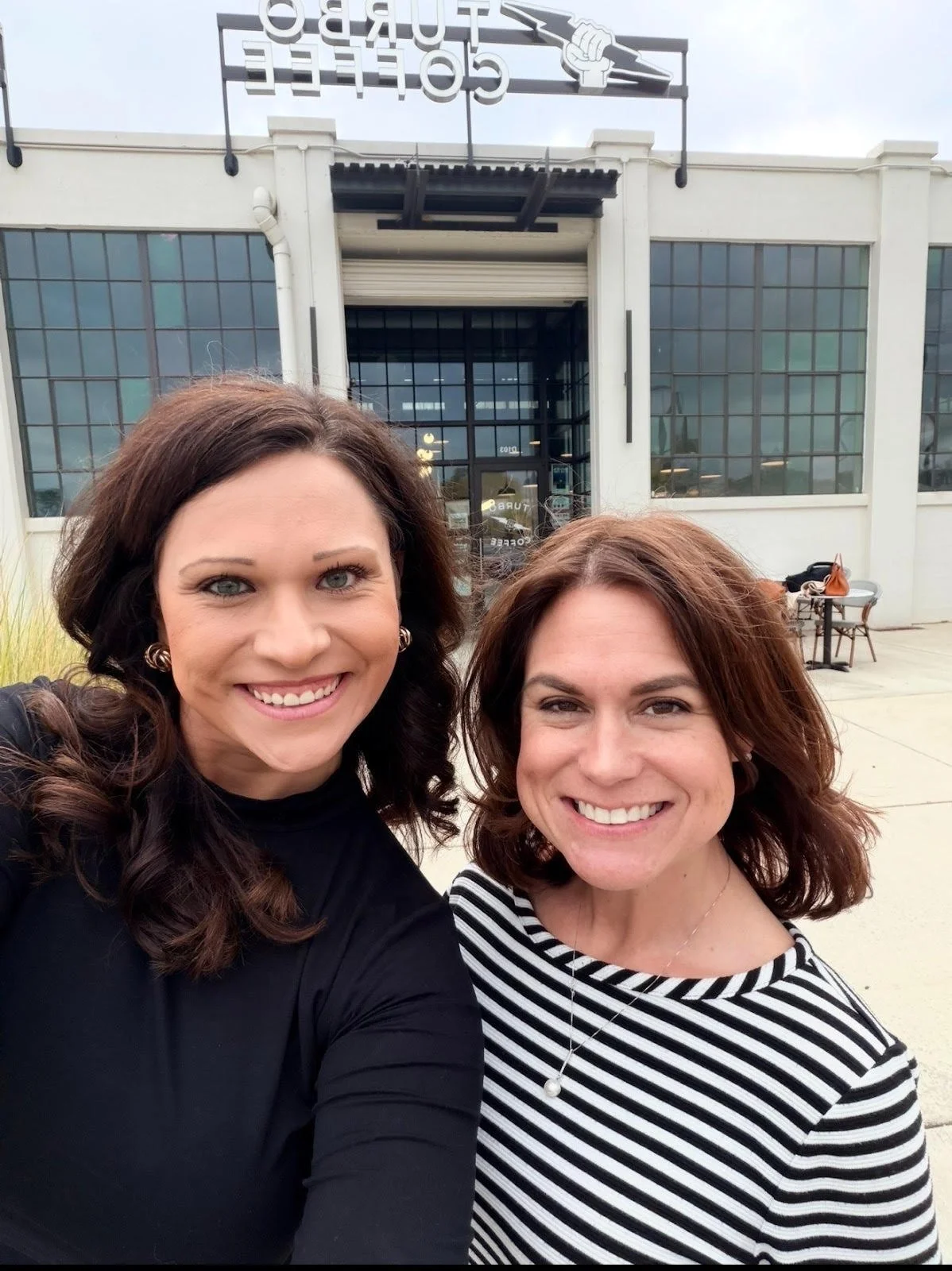 Two women smiling and taking a selfie outside a Coffee & Curios restaurant.