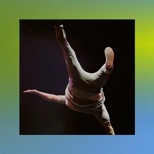A person performing a handstand or acrobatic move against a black background in a dark setting.