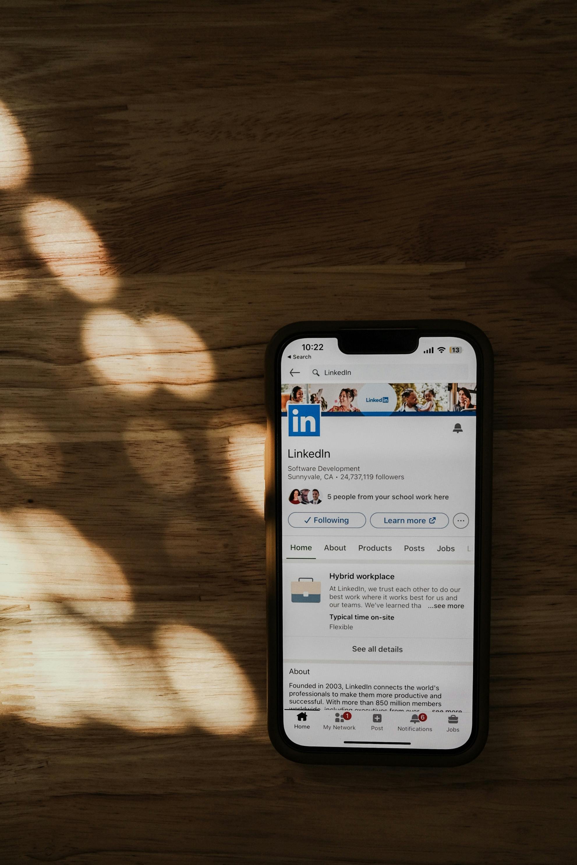 Smartphone on wooden table displaying LinkedIn profile page with a shadow of circular shapes cast across the table