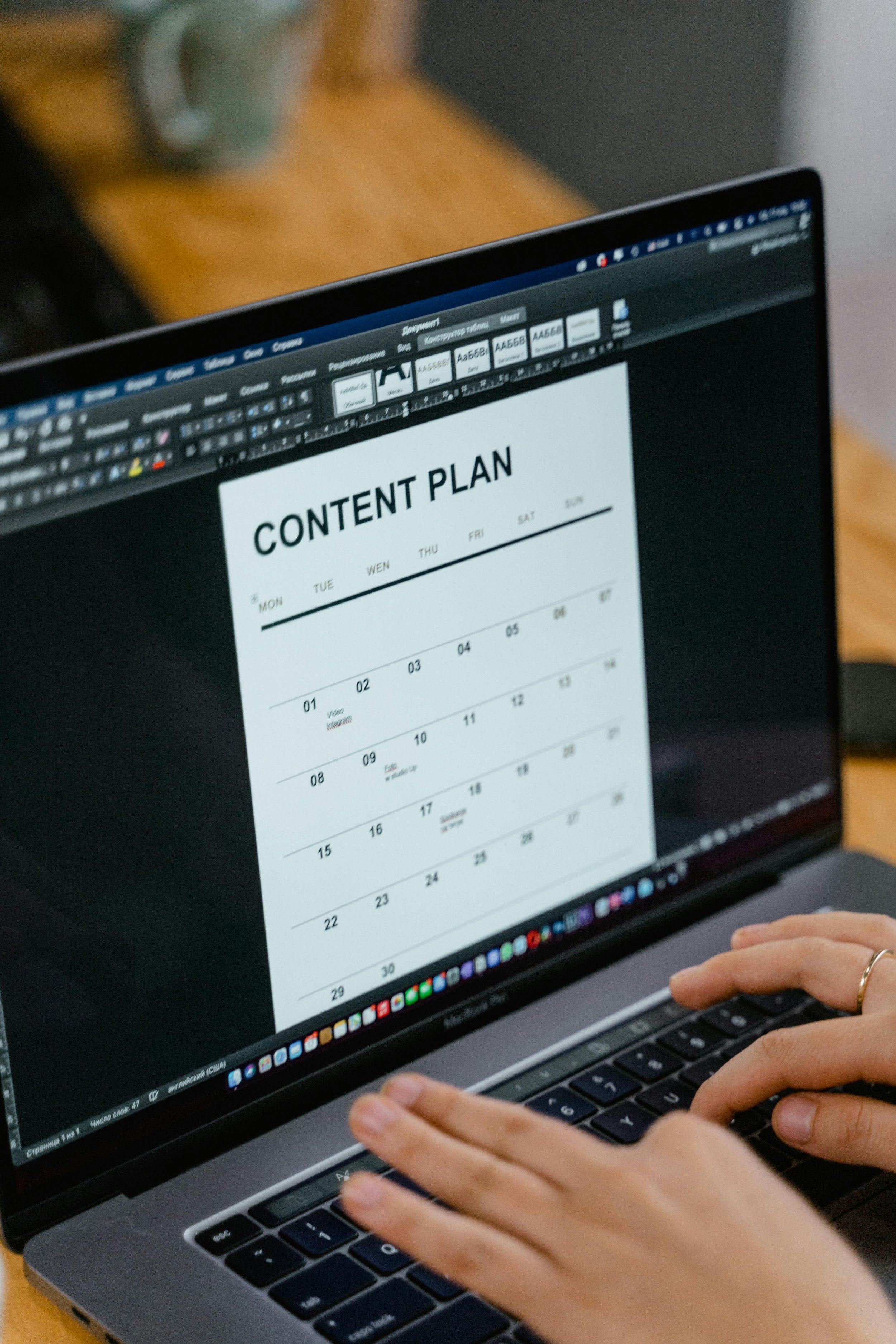 A person working on a laptop with a content plan displayed on the screen.