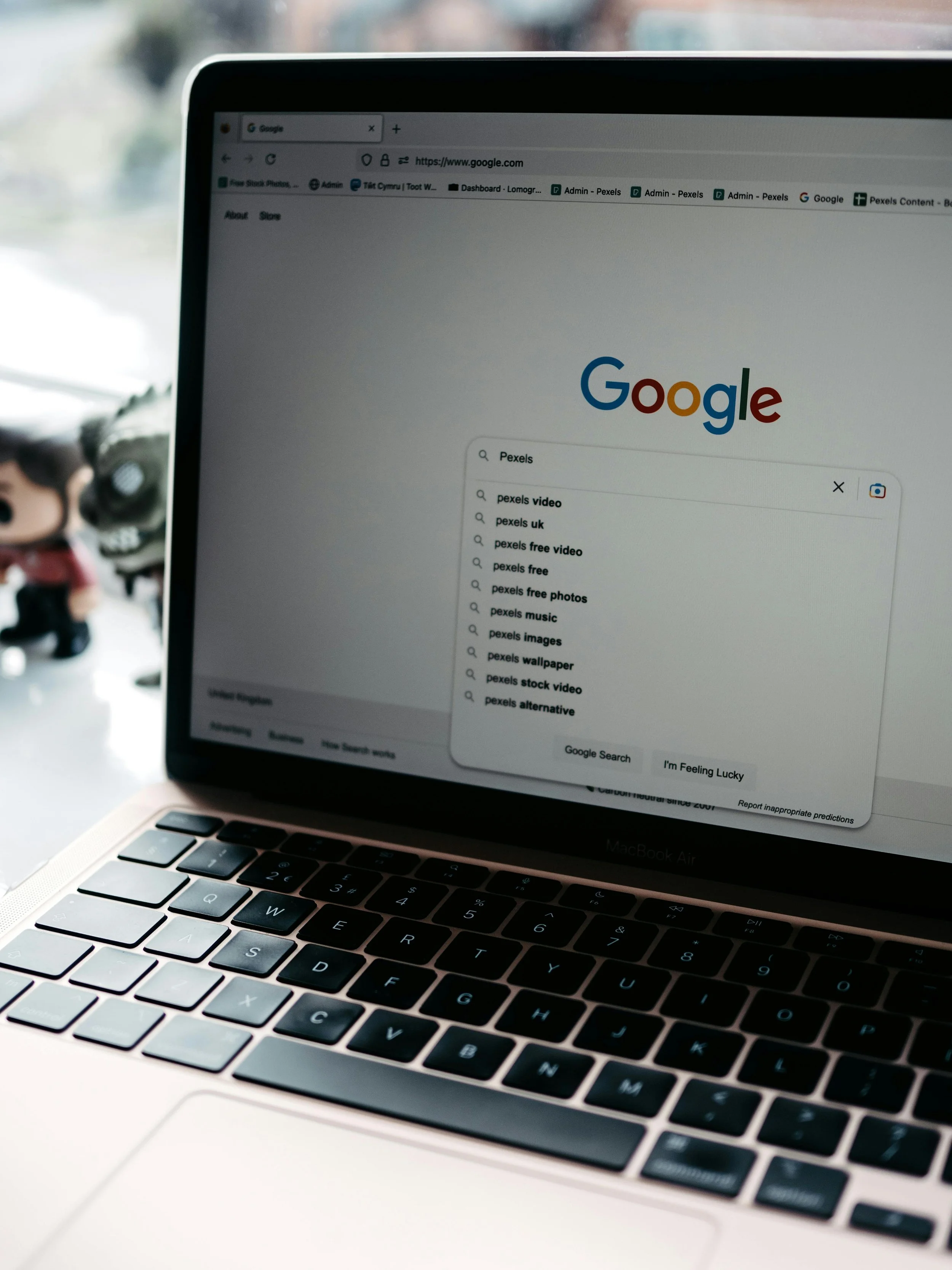 Laptop screen displaying the Google homepage with a search bar open, searching for Pexels, with various related search suggestions.