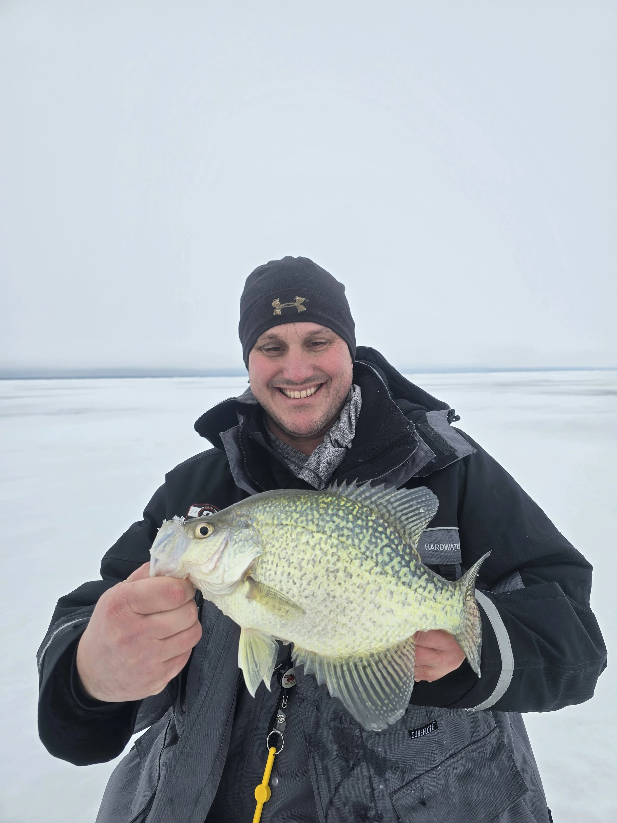 Man smiling and holding a large fish on a snowy landscape background during winter