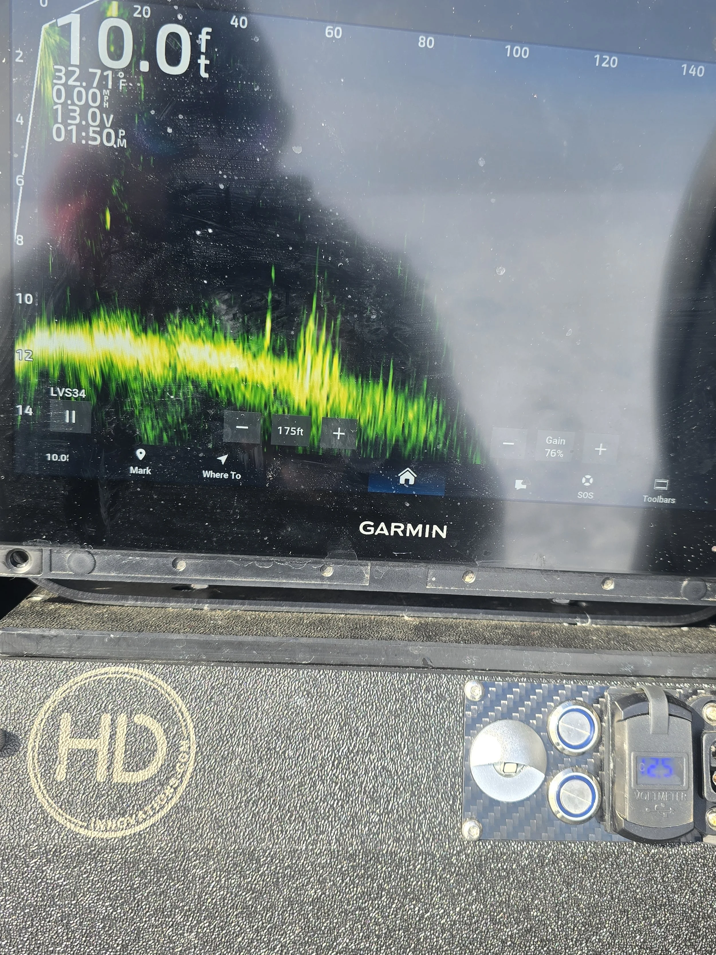 Close-up of a Garmin marine device display showing depth at 10.0 feet, water temperature 32.71°F, voltage 13.0V, and current time 1:50 PM. Part of a boat's dashboard with a 'HID' label, a fuse, and various controls.