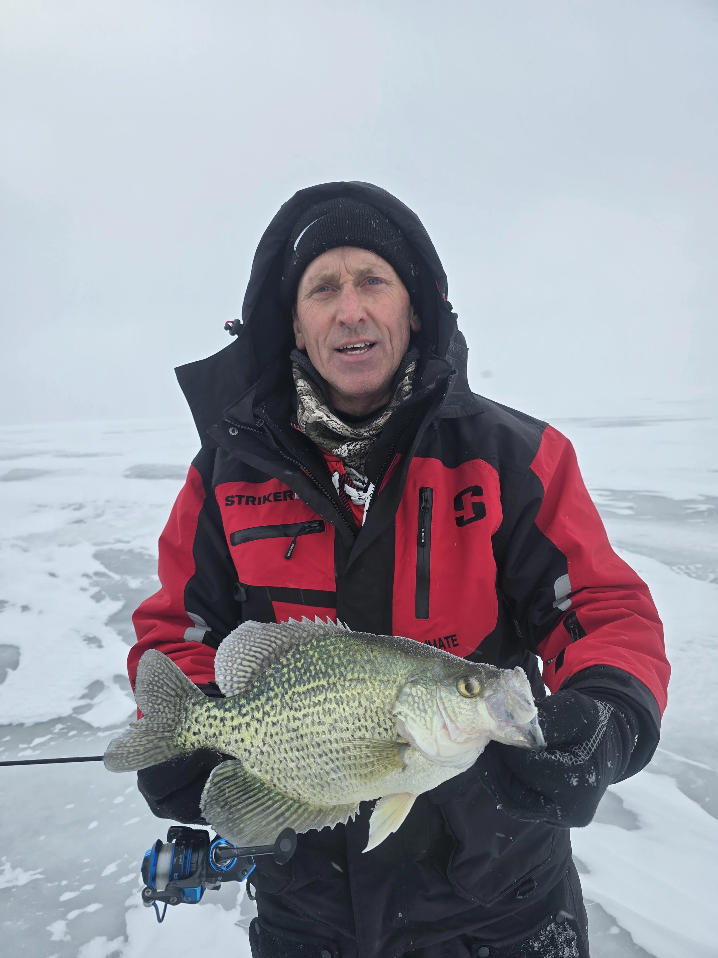 A man in winter clothing holding a large fish on a snowy landscape with a foggy sky.