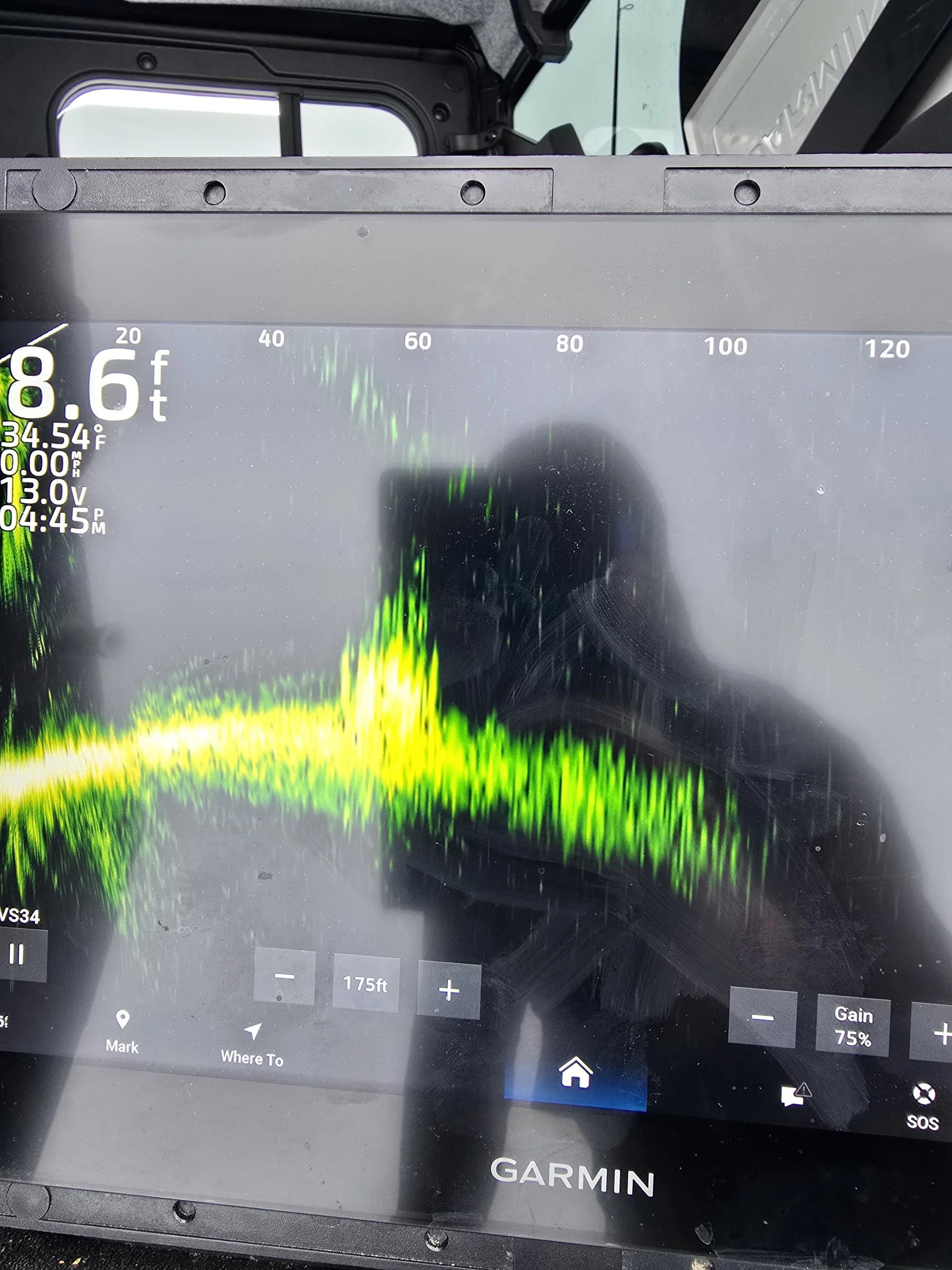 A Garmin GPS device displaying a sonar screen with colorful readings, indicating underwater topography or fish activity. The screen shows depth, temperature, and other navigation information.