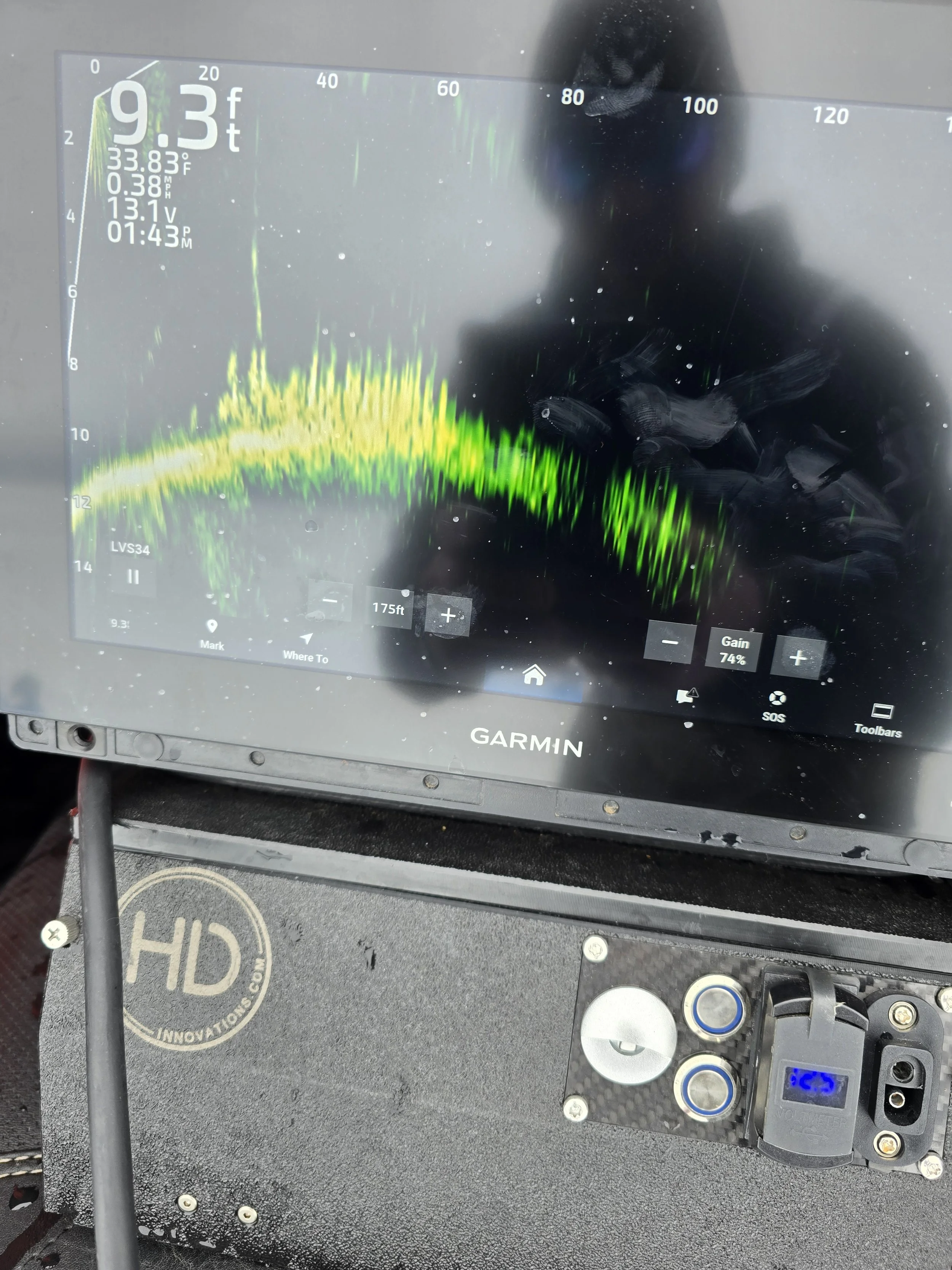 Close-up of a fishfinder display showing underwater terrain and fish, with water temperature 33.83°F, speed 0.38 MPH, voltage 13.1V, time 1:43 AM, and depth 9.3 feet.