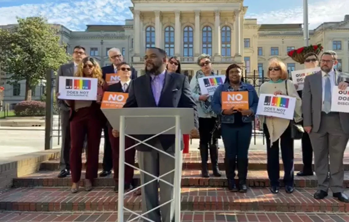 Group of people protesting outside a government building, holding signs with messages of opposition and support for LGBTQ rights.