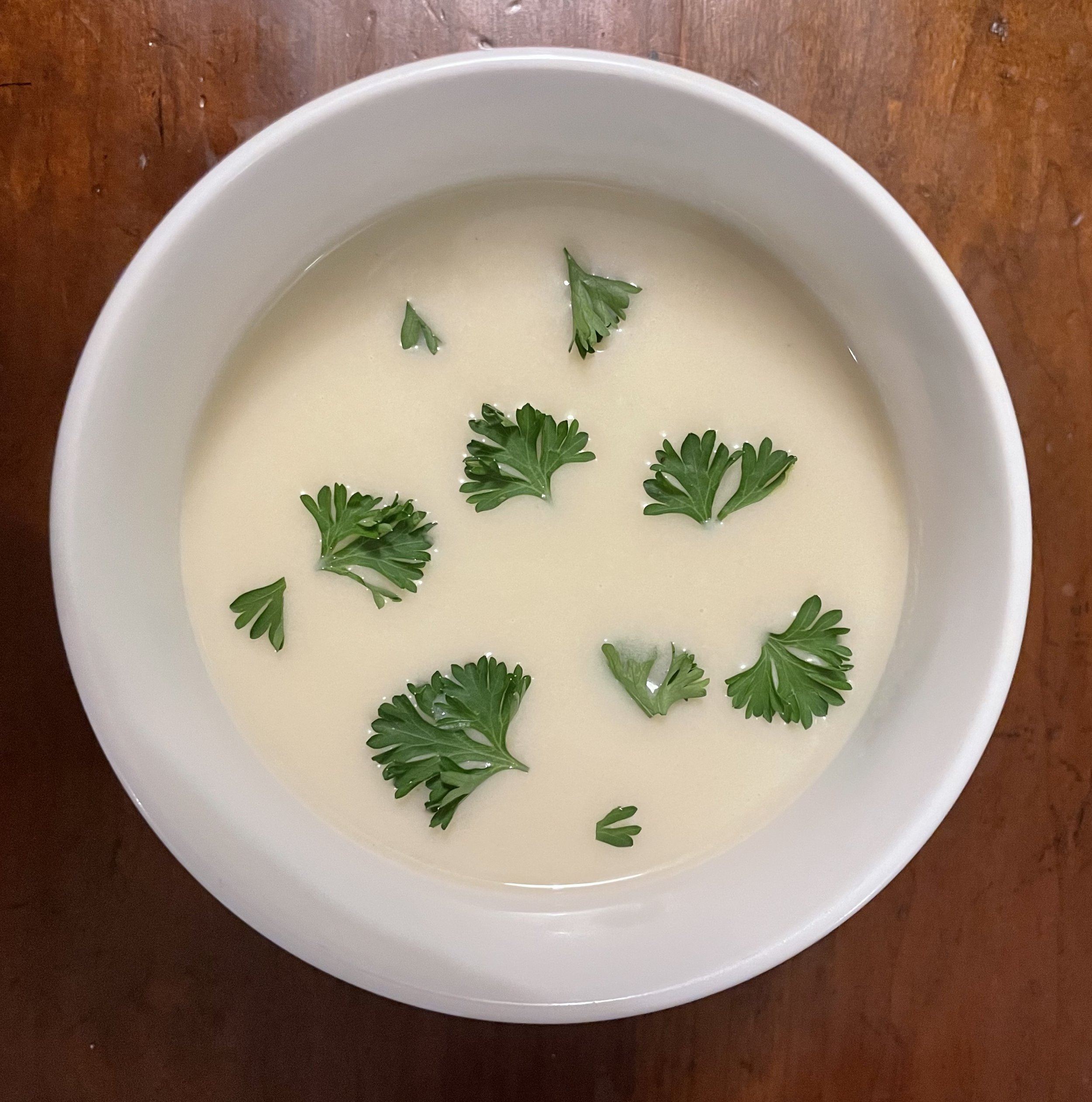 Bowl of creamy potato leek soup garnished with fresh parsley leaves on a wooden surface.