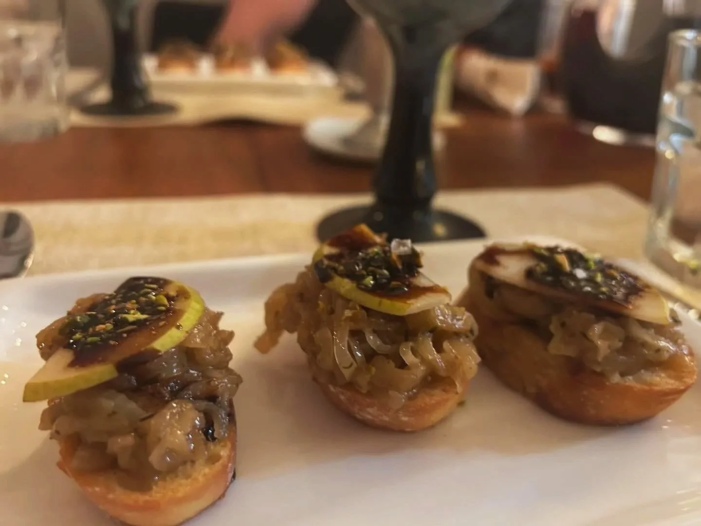 Three slices of baguette topped with caramelized onions, sliced figs, and a balsamic glaze with crushed pistachios, served on a white plate.