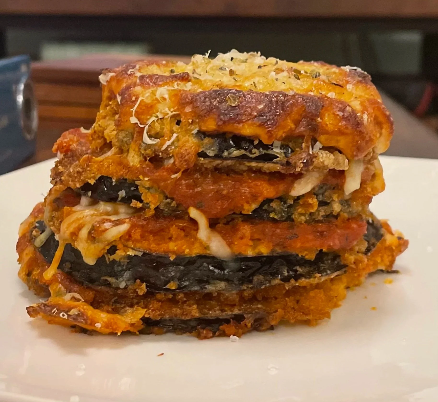A slice of layered eggplant Parmesan with cheese and tomato sauce on top, served on a white plate.